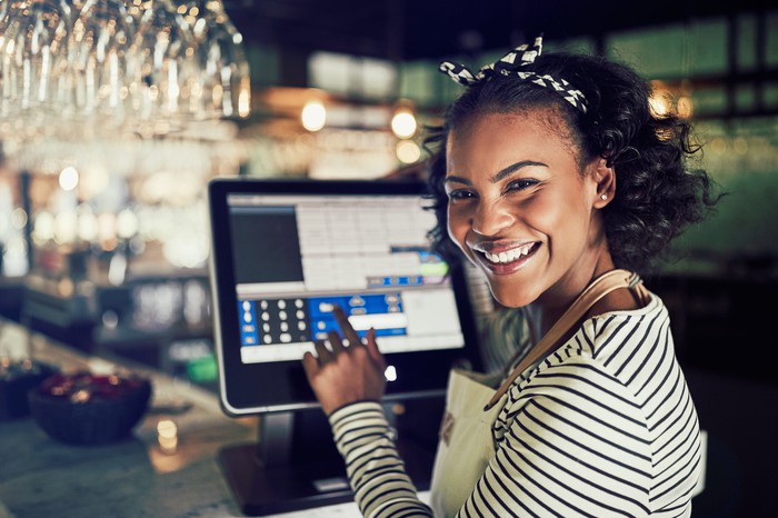 A smiling young retail associate using a point-of-sale touchscreen computer. 